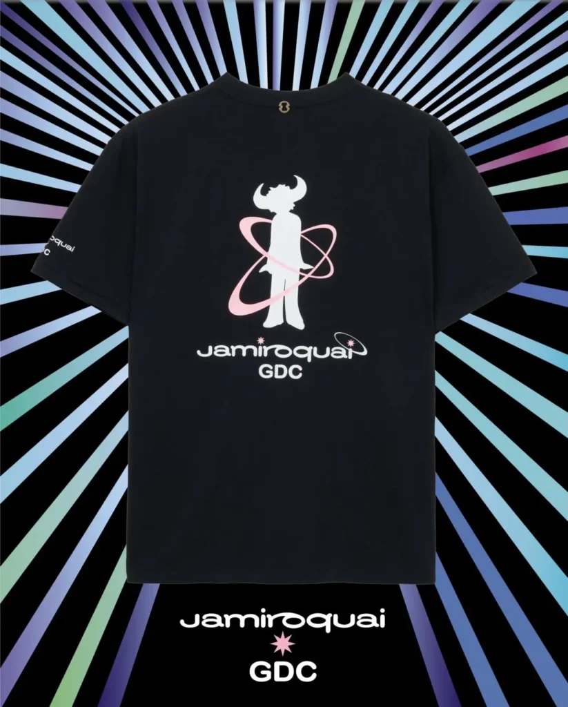 Front-facing product shot of the black Jamiroquai x GDC T-shirt. A pink starburst logo appears on the chest, complemented by subtle sleeve branding and a clean min present