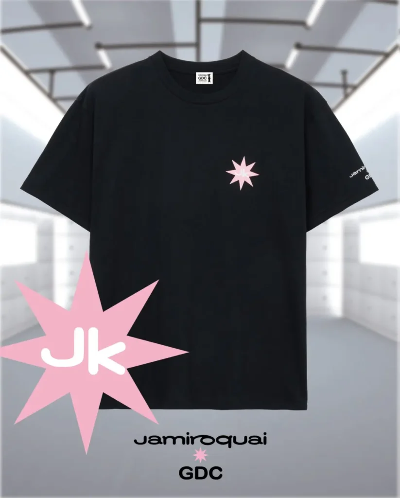 Product image of the white Jamiroquai x GDC T-shirt displayed against a vibrant radial graphic backdrop. The back print combines the buffalo-man icon, pink orbital rings, and dual-brand logo treatment