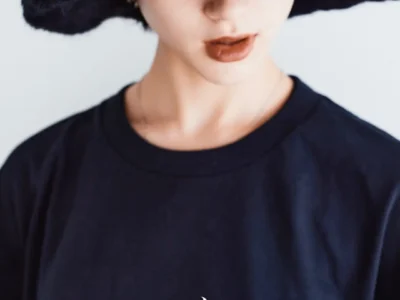 Close-up portrait of a model wearing a black Jamiroquai x GDC T-shirt and oversized fuzzy bucket hat. The shirt’s chest graphic combines the iconic buffalo-man logo with a soft pink orbital motif and starburst accent