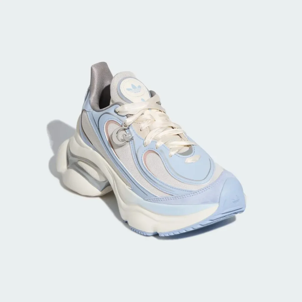Three-quarter front angle of a retro-futuristic adidas runner with light blue overlays, white mesh underlays, cream laces, and a thick cushioned sole designed for a bold lifestyle aesthetic