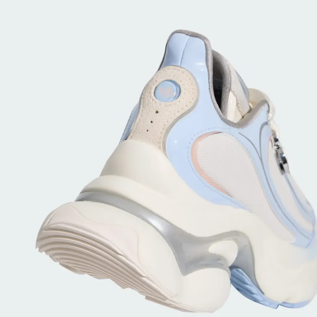 Close-up heel view of the Adidas shoe emphasizing the oversized cream sole unit, translucent silver midsole structure, pastel blue heel tab, and layered materials throughout the design
