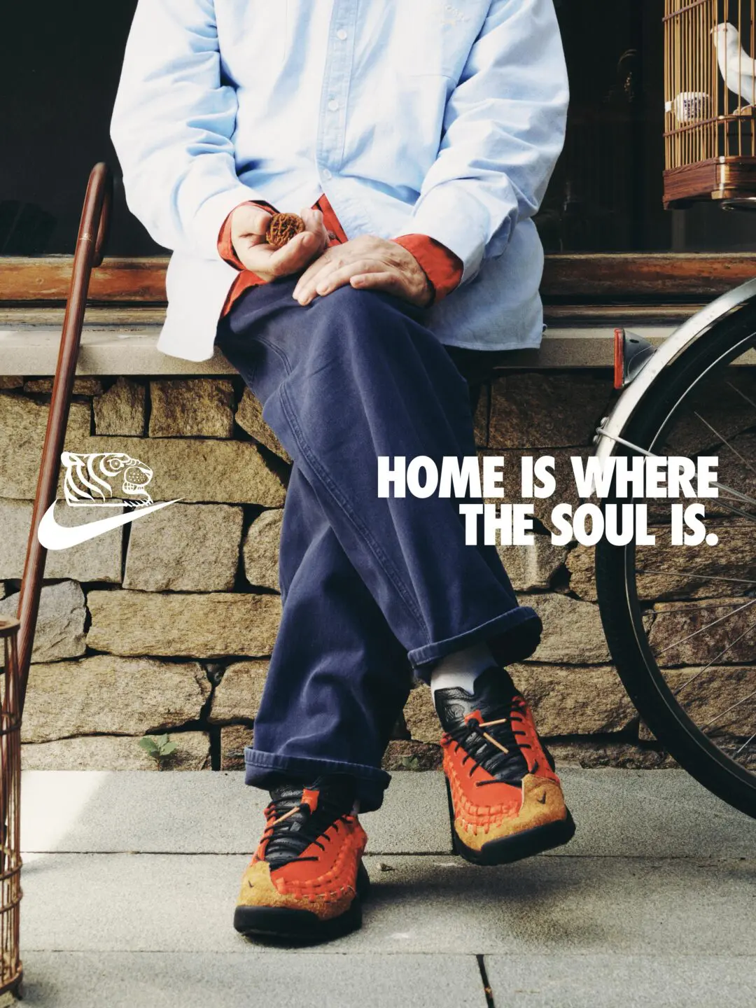 SOULGOODS x Nike Homescape Woven SP Chile Red HM6961-600 lifestyle shot with model in blue shirt and dark pants, tiger logo, and 'Home is Where the Soul Is' campaign tagline