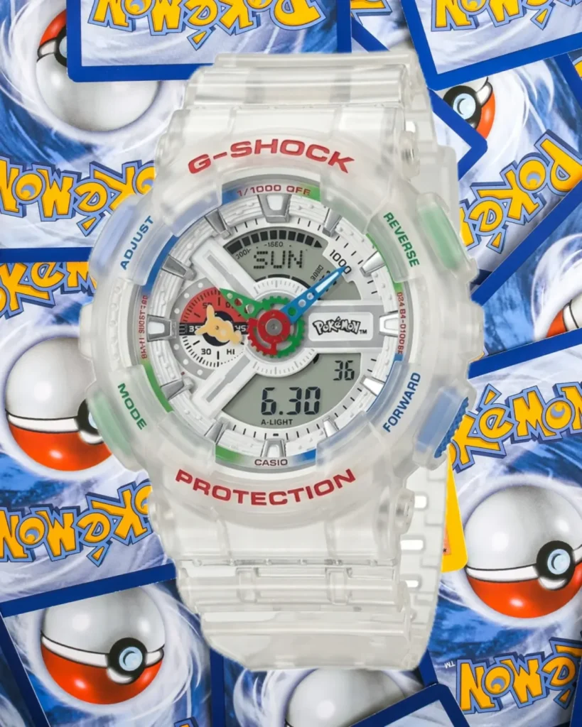 A close-up product shot of the Pokémon x G-SHOCK GA-110 collaboration watch featuring a transparent resin case and strap. The oversized analog-digital dial showcases colorful Pokémon-inspired details, including blue and green hands, multicolored accents, and a Pokémon logo at the center. Red “G-SHOCK” and “PROTECTION” branding stand out on the bezel, while translucent side buttons add a futuristic touch. The watch is displayed against a backdrop of scattered Pokémon trading cards and Poké Ball graphics, emphasizing the crossover’s nostalgic gaming appeal and collectible status