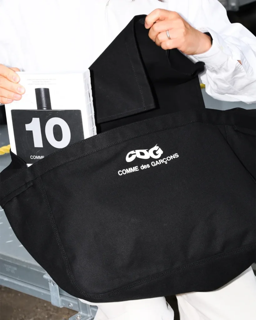 Close-up of a black COMME des GARÇONS CDG tote bag filled with books and personal items, demonstrating its spacious interior and sturdy canvas construction