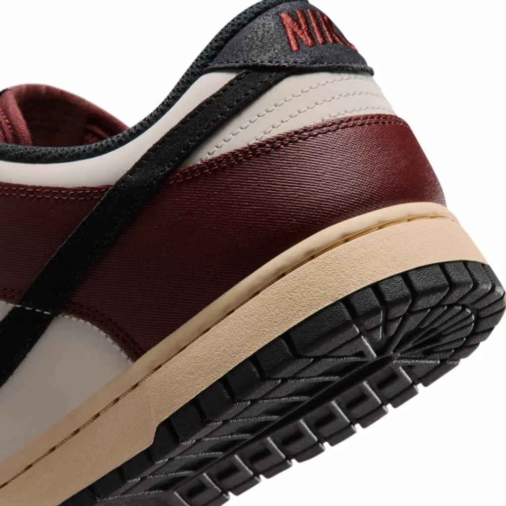 Close-up of the burgundy Nike Dunk Low heel emphasizing burgundy textured heel overlay, cream leather panel, black suede heel tab with embroidered Nike logo, and aged cream mid