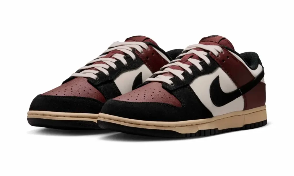 Angled pair shot of the burgundy, sail, and black Nike Dunk Low highlighting perforated burgundy toe boxes, cream laces, black suede mudguards, and vintage-inspired cream mid