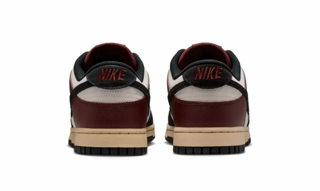 Rear heel view of the burgundy Nike Dunk Low featuring embroidered Nike branding on black suede heel tabs, burgundy heel overlays, sail heel panels, and vintage cream mid