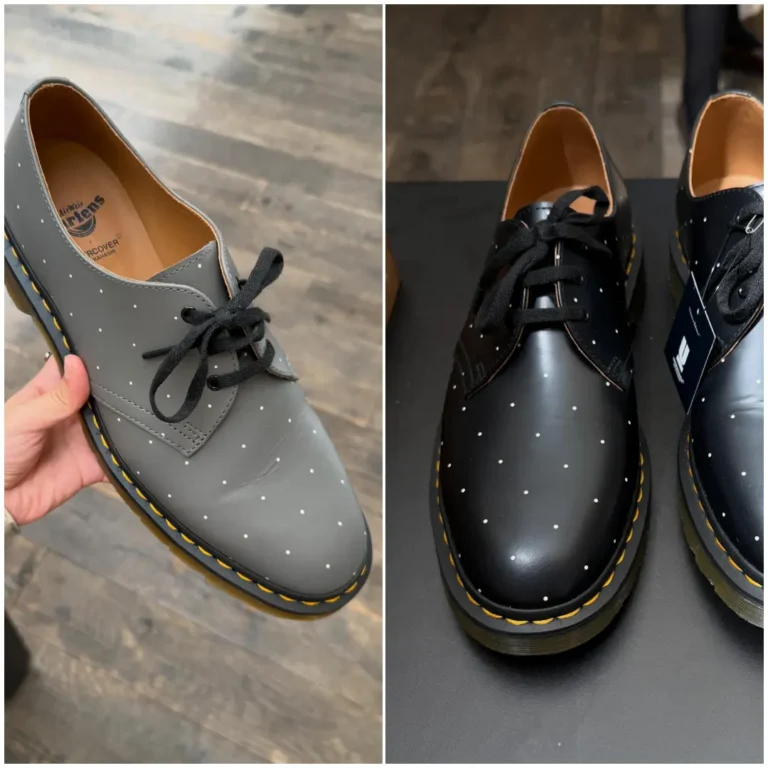 Hand holding a gray Dr. Martens 3-eye derby shoe featuring a minimalist white polka-dot pattern across the leather upper, black laces, signature yellow welt stitching, and a translucent AirWair sole against a wooden floor background