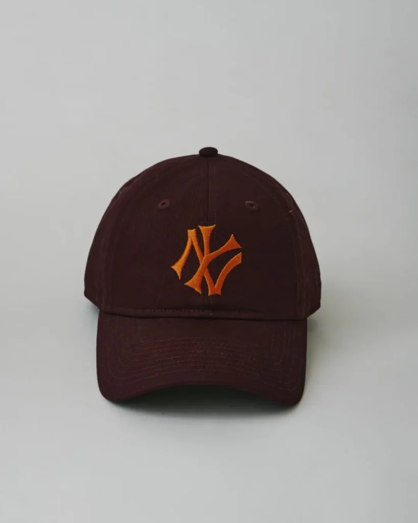 Front view of a deep burgundy New York Yankees cap accented by a vibrant orange embroidered NY logo and curved brim sil