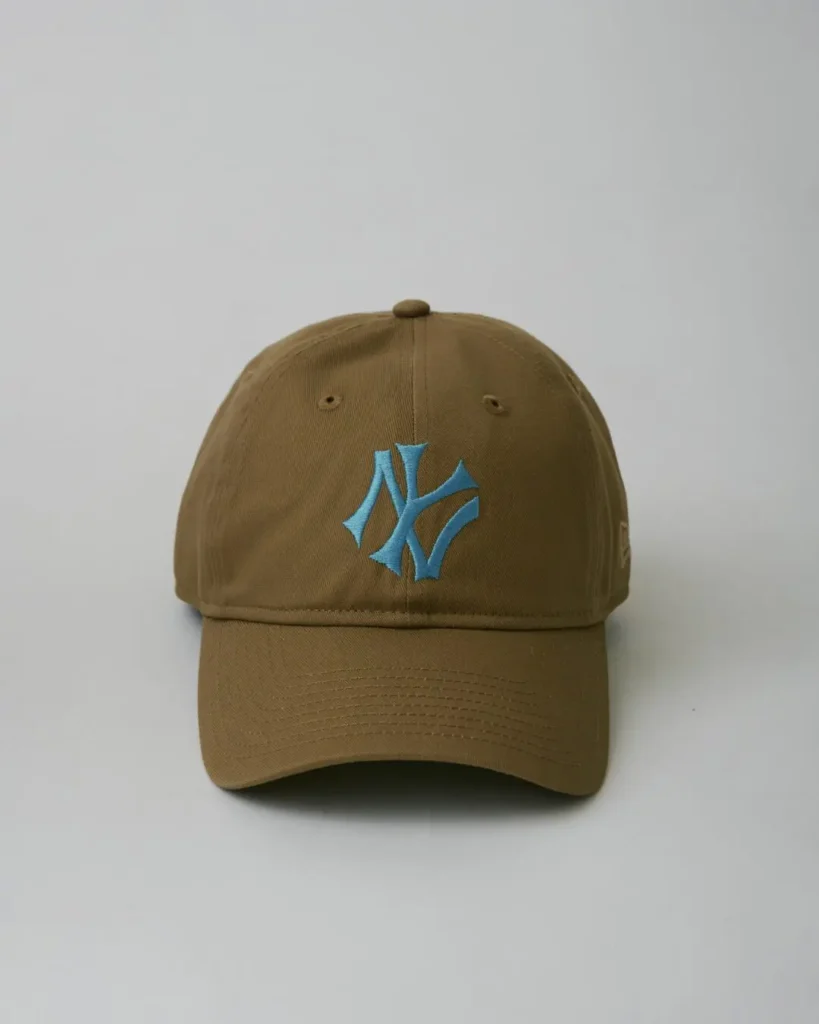 Front view of a khaki New York Yankees cap featuring a bright sky-blue embroidered NY logo, structured crown, and curved visor