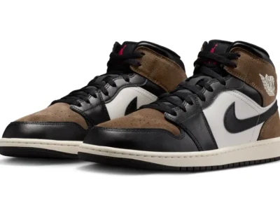Air Jordan 1 Mid “Black/Palomino” sneakers displayed in a three-quarter view, featuring premium brown suede overlays, black leather panels, sail midsoles, and subtle red Jumpman accent