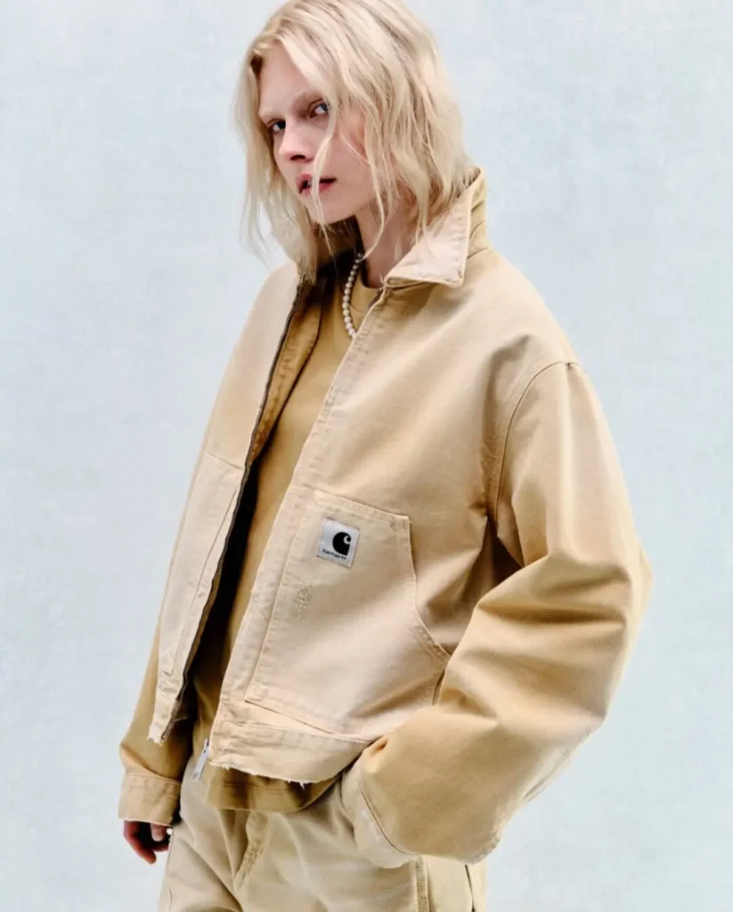 Model styled in a cropped beige workwear jacket and matching trousers layered over tonal separates, showcasing Carhartt WIP’s washed canvas textures and relaxed silhouette