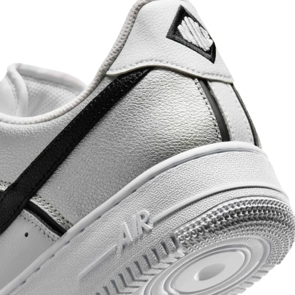 Detailed heel close-up showing the metallic silver leather texture, black Swoosh extension, embroidered heel branding, and the classic white Air Force 1 mid