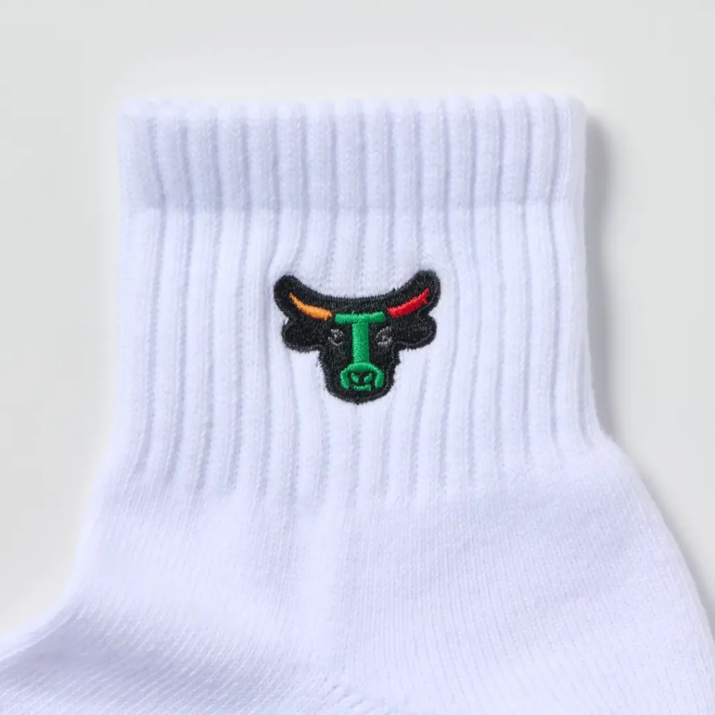 Close-up of a white ribbed quarter-length sock featuring an embroidered bull-head logo near the cuff. The textured knit construction and colorful embroidery stand out against the bright white fabric