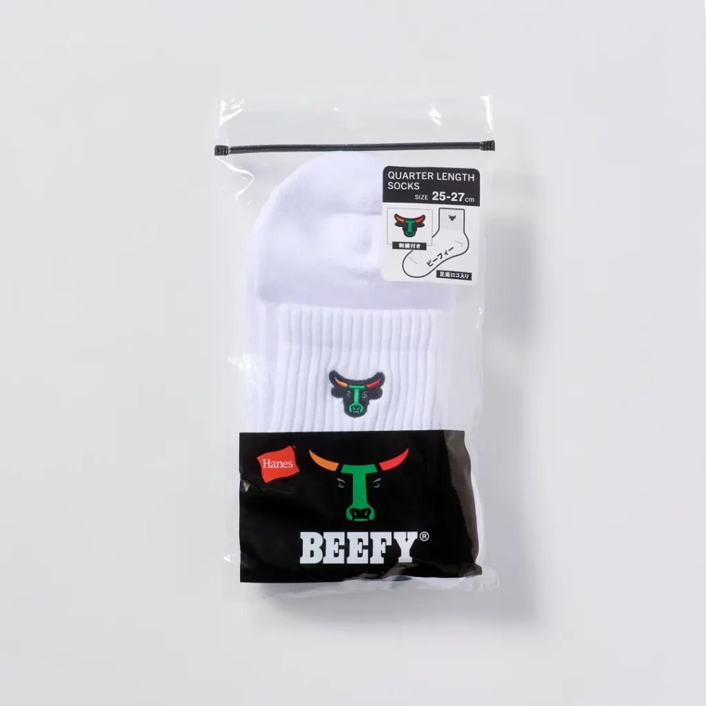 Packaged white Hanes BEEFY quarter-length socks displayed in a clear zip-top bag with branded labeling. The visible embroidered bull-head logo and bold packaging graphics reinforce the collision's identity