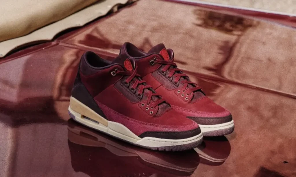 Pair of Air Jordan 3 Low BIN23 shoe displayed on a reflective burgundy surface, featuring premium wine-red leather and suede construction with aged cream midsoles and refined luxury detail