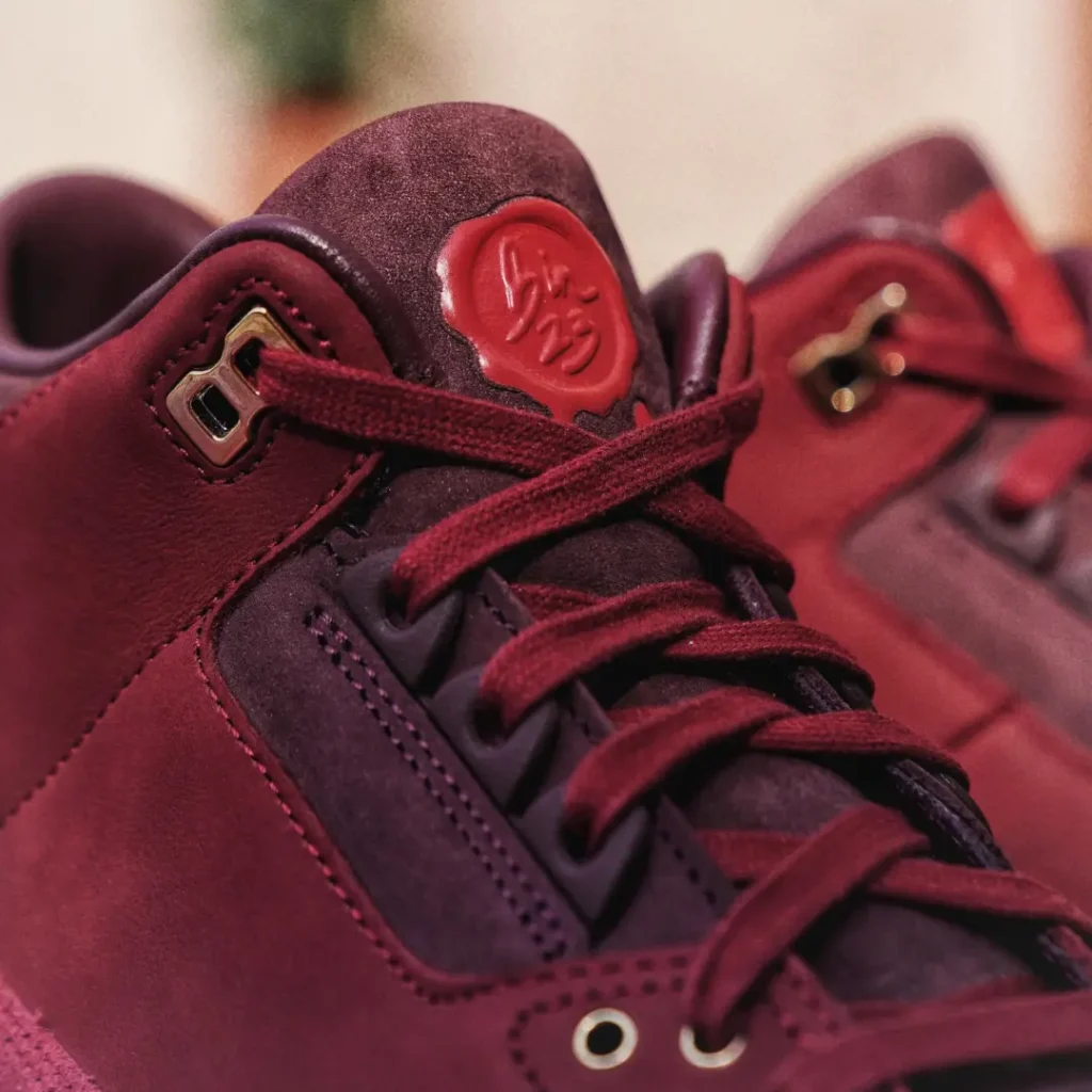 Close-up of the Air Jordan 3 Low BIN23 tongue showcasing rich burgundy suede, wax-seal-inspired BIN23 branding, tonal laces, and metallic eyelet