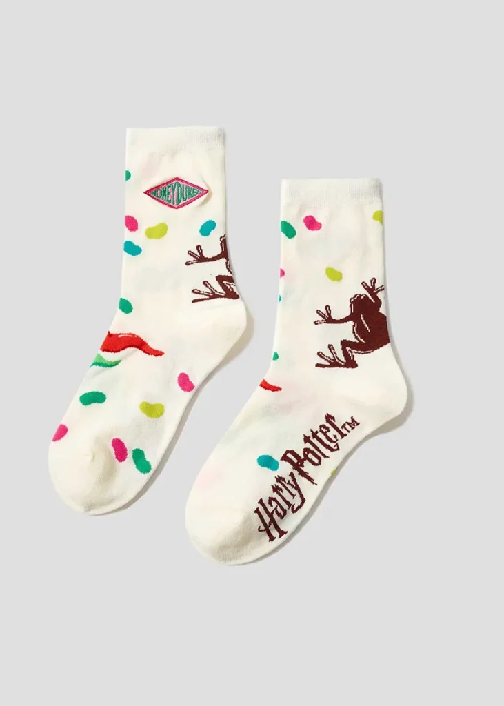 Cream-colored Harry Potter-themed socks decorated with colorful candy motifs, a Honeydukes-inspired logo patch, chocolate frog graphics, and Harry Potter wordmark detail