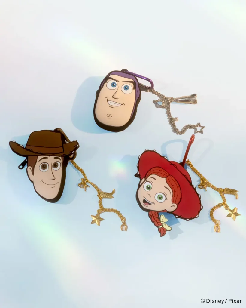 Character face pouch charms featuring Woody, Jessie, and Buzz Lightyear with metallic western-themed chain accents and collectible accessory detail