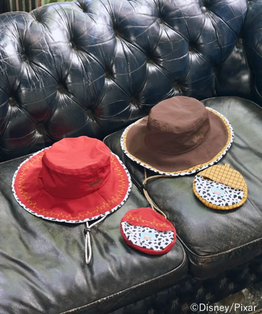 Toy Story-inspired bucket hats in Jessie red and Woody brown featuring western-themed embroidery and cow-print detailing photographed on a vintage leather sofa