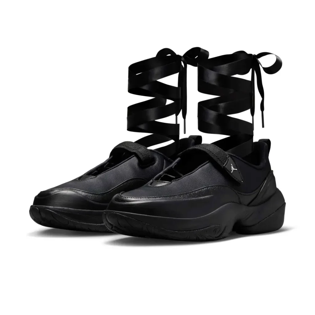 Air Jordan women’s black ballet-inspired shoe featuring oversized satin ribbon laces wrapped up the ankles, shown in a three-quarter studio view against a light gray background