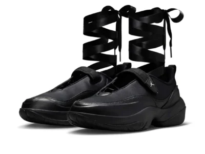 Air Jordan women’s black ballet-inspired shoe featuring oversized satin ribbon laces wrapped up the ankles, shown in a three-quarter studio view against a light gray background