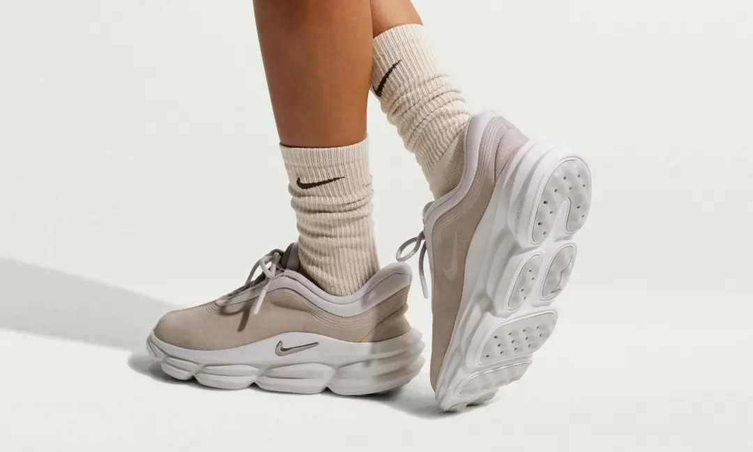 Nike 24.7 "Cream/Phantom" recovery shoes worn with ribbed Nike crew socks, showcasing the neutral-toned upper, sculpted foam pod cushioning, and slip-on-inspired comfort design against a clean studio background