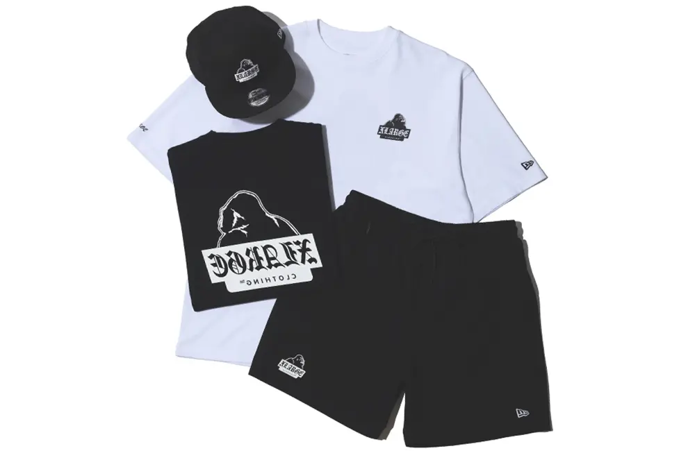 Flat lay of the XLARGE x New Era capsule featuring a black snapback cap, black shorts, and black-and-white graphic T-shirts with co-branded streetwear logo