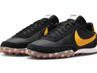 Nike Waffle Trainer 2-style sneaker in black nylon with vibrant golden-yellow Swooshes, suede overlays, and a translucent waffle outsole shown in a three-quarter view