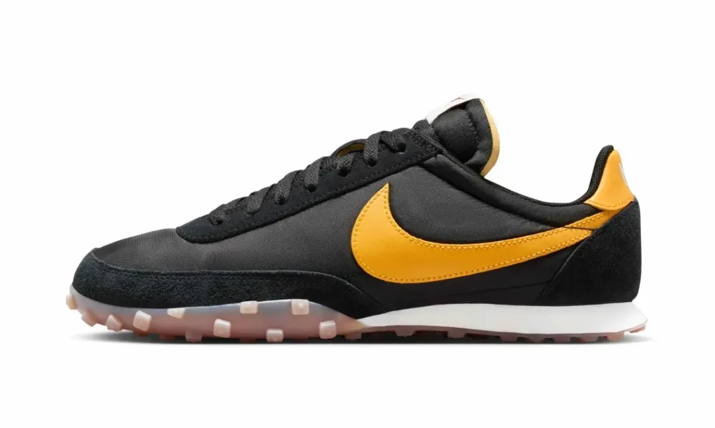 Side profile of a Nike retro runner featuring a black textile upper, golden-yellow leather Swoosh, suede mudguard, and classic low-profile sil