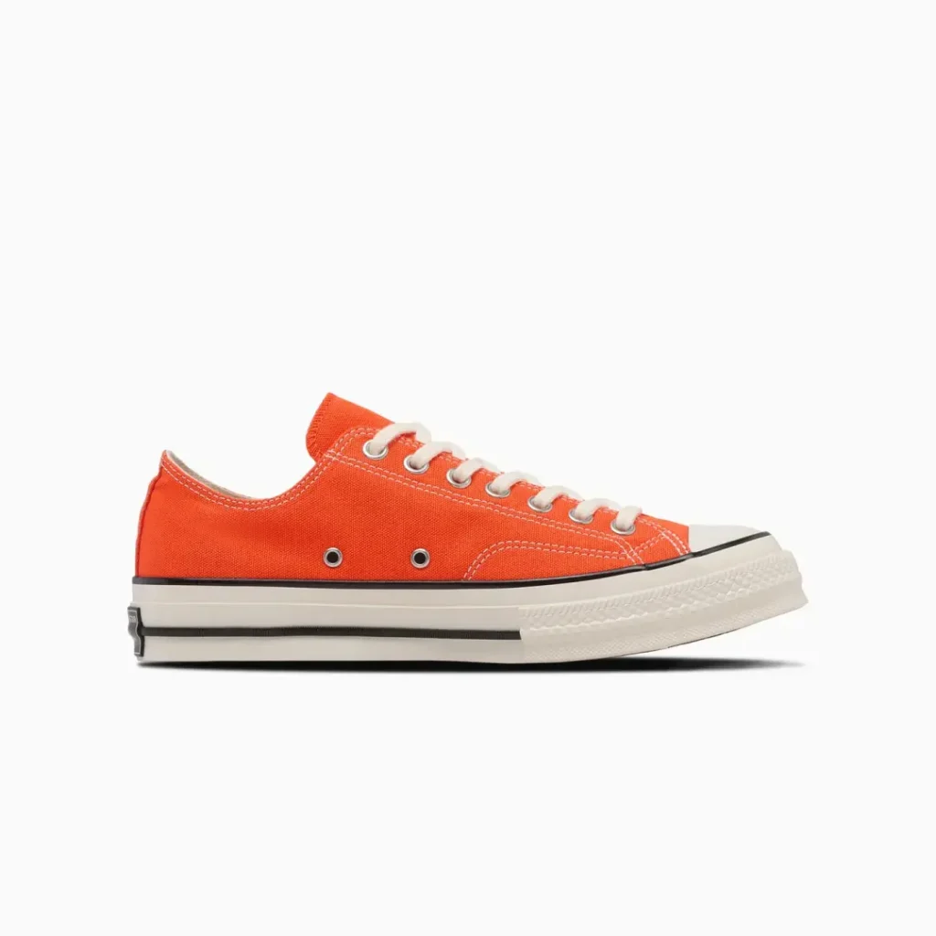 Side profile of the Converse Chuck Taylor All Star low-top shoe in bright orange canvas with cream laces, off-white rubber sole, and classic black foxing stripe