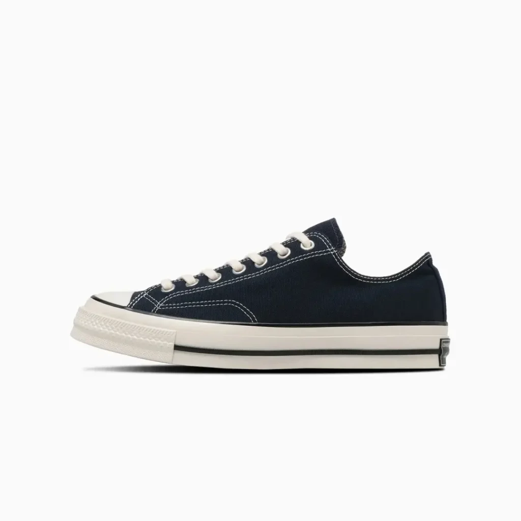 Side profile of the navy Converse Chuck Taylor All Star low-top shoe showcasing dark canvas material, white stitching, cream laces, and a classic sole unit