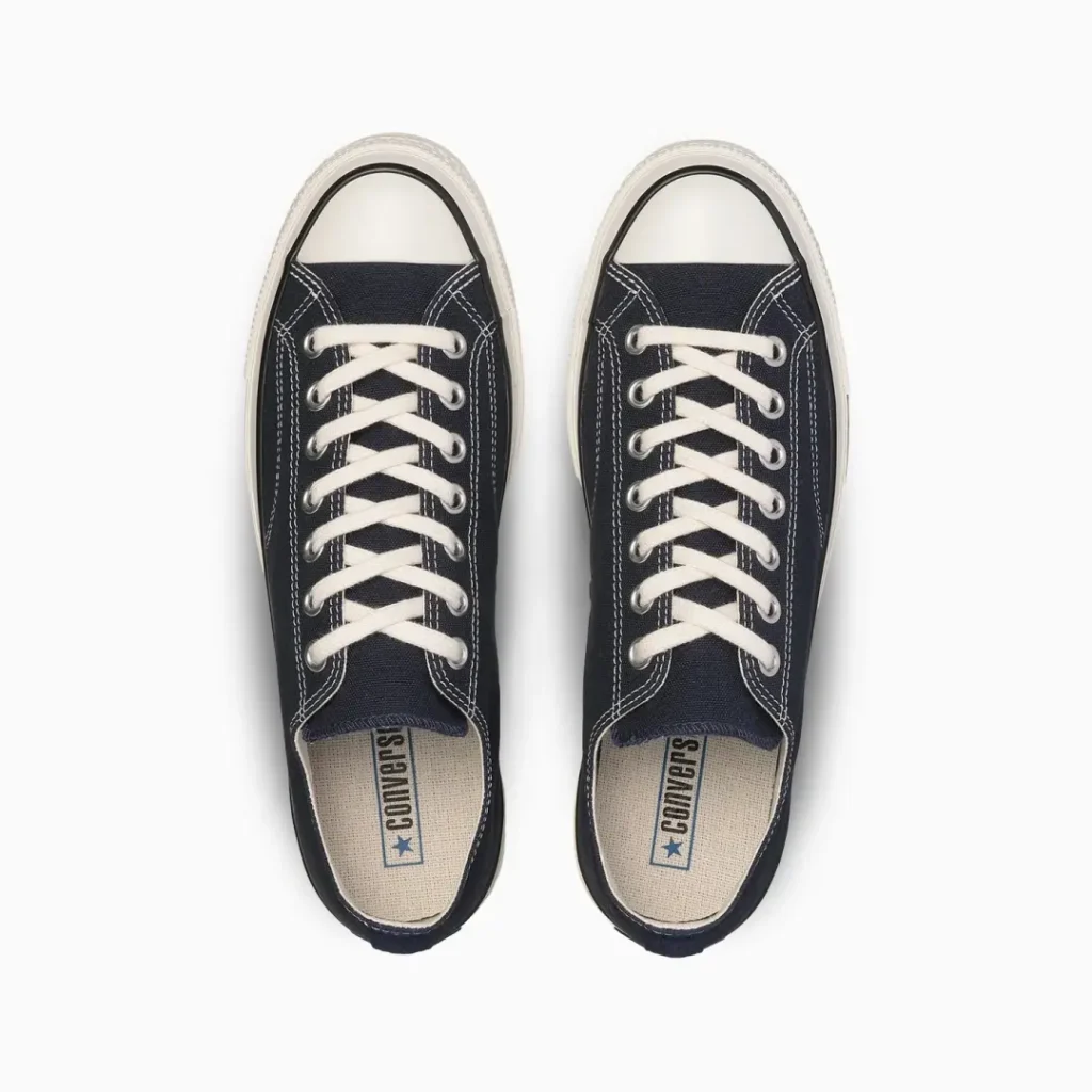 Top-down view of navy Converse Chuck Taylor All Star low-top shoe showcasing neatly laced cream shoelaces, canvas uppers, cushioned footbeds, and signature rubber toe cap