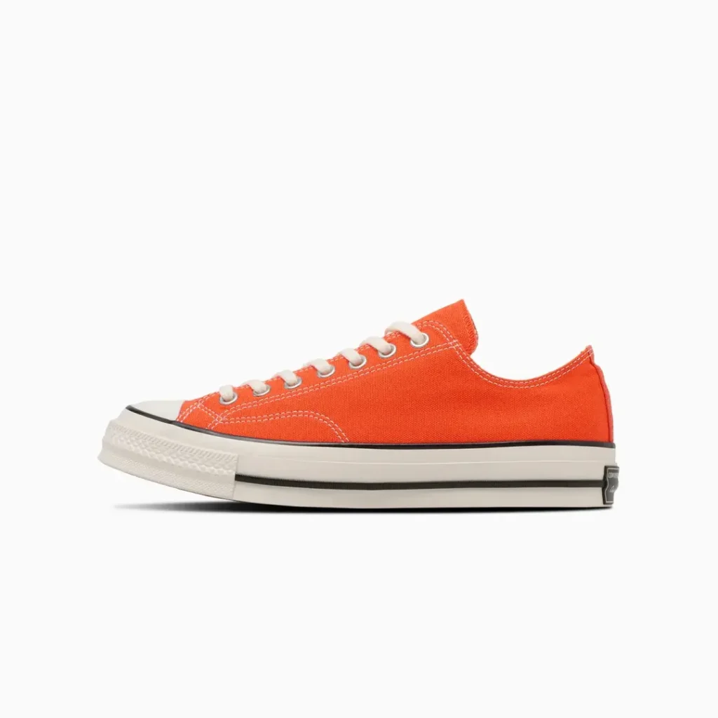 Side profile of the Converse Chuck Taylor All Star low-top shoe in bright orange canvas with cream laces, off-white rubber sole, and classic black foxing stripe