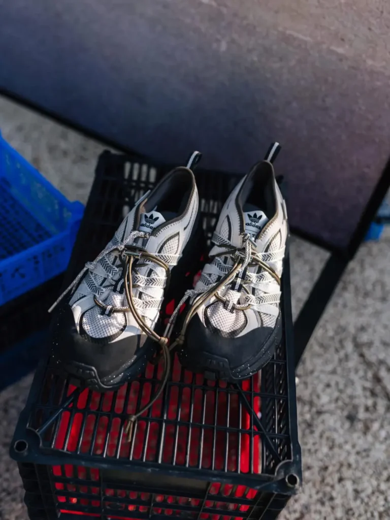 White and black adidas outdoor shoe displayed atop a black plastic crate, featuring chunky speckled soles and hiking-inspired lace
