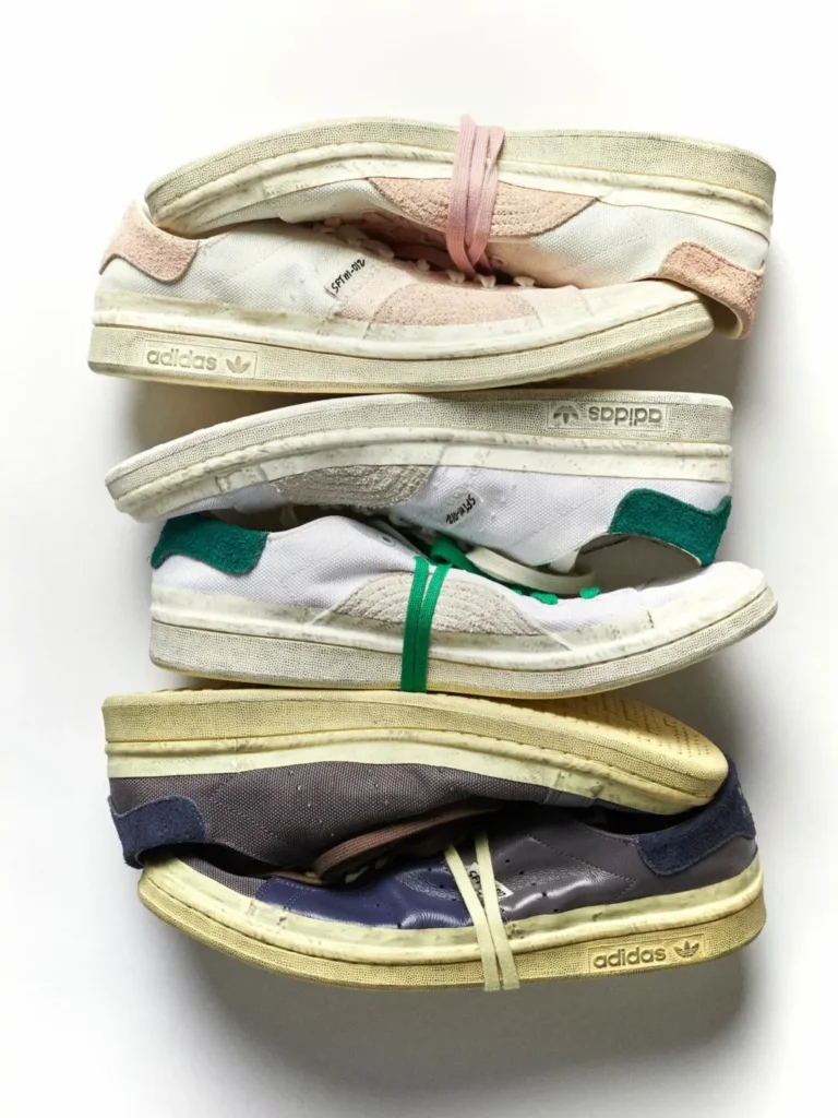 Three stacked pairs of weathered adidas Stan Smith sneakers in pink, green, and navy colorways displayed against a white backdrop
