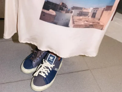 Navy adidas shoe placed beneath a printed graphic shirt, highlighting their worn canvas construction and mismatched lace tincture