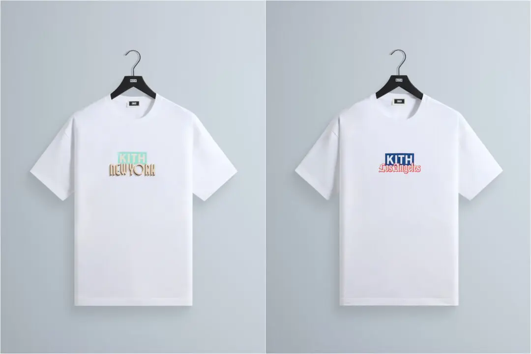 White Kith Tee displayed on a black hanger against a light gray backdrop, featuring a pastel mint Kith logo above a vintage-inspired “New York” wordmark in metallic cream and gold tones. The min presentation highlights the clean silhouette and city-exclusive graphic treatment