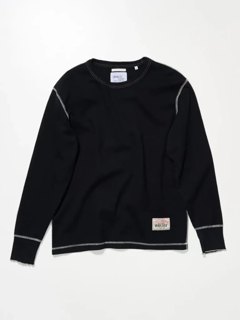 Black long-sleeve crewneck top with contrast white stitching, raw-edge detailing, and collective workshop label accent