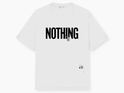 White short-sleeve T-shirt with a monochrome back graphic of Shizuka from Doraemon standing in profile and holding a gadget. Vertical “MUCH LOVE” typography and small technical-style text details add a contemporary streetwear show