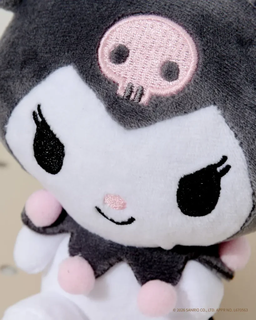 Close-up of a Kuromi plush mascot keychain highlighting the signature skull emblem, embroidered eyes, pink nose, and soft plush construction