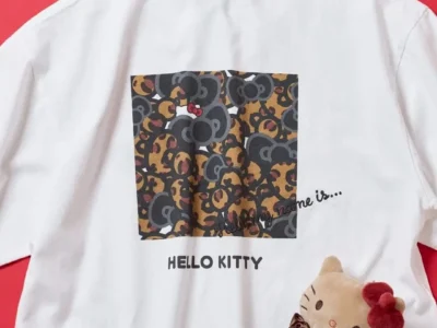 White Hello Kitty graphic T-shirt featuring a small embroidered Hello Kitty motif on the chest and a camouflage-inspired character print across the back panel