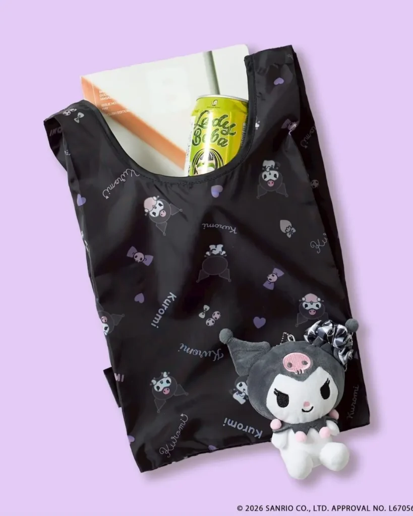 Black Kuromi foldable shopping bag with lavender accents, all-over character print, and coordinating plush mascot keychain attached to the handle