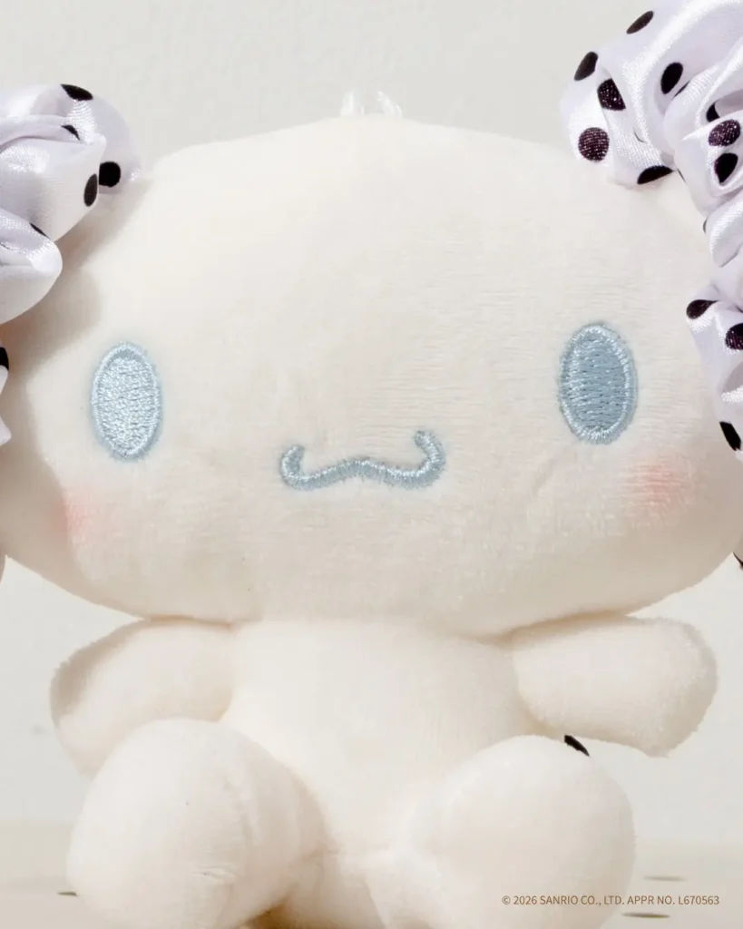 Detailed portrait of a Cinnamoroll plush charm with soft white fabric, embroidered blue facial features, rosy cheeks, and polka-dot ribbon accent