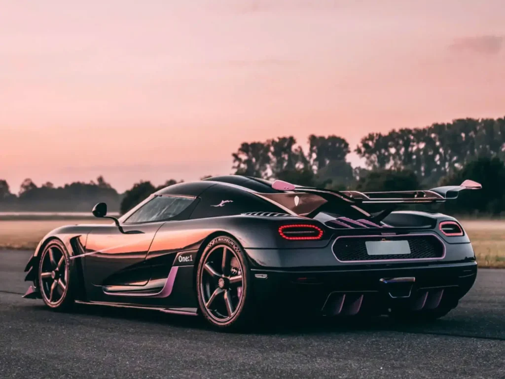 Rear three-quarter view of the Koenigsegg One:1 hypercar at sunset, showcasing its carbon-fiber bodywork, active rear wing, aerodynamic diffuser, and signature LED taillight