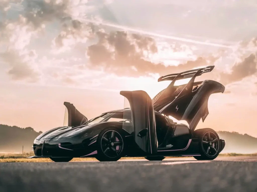 Koenigsegg One:1 hypercar photographed with both dihedral doors raised at sunrise, emphasizing its dramatic silhouette, aerodynamic profile, and track-bred design language