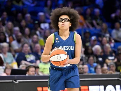 Olivia Miles in her Minnesota Lynx blue jersey holding the basketball, poised for action with signature afro and glasses during the 2026 WNBA season