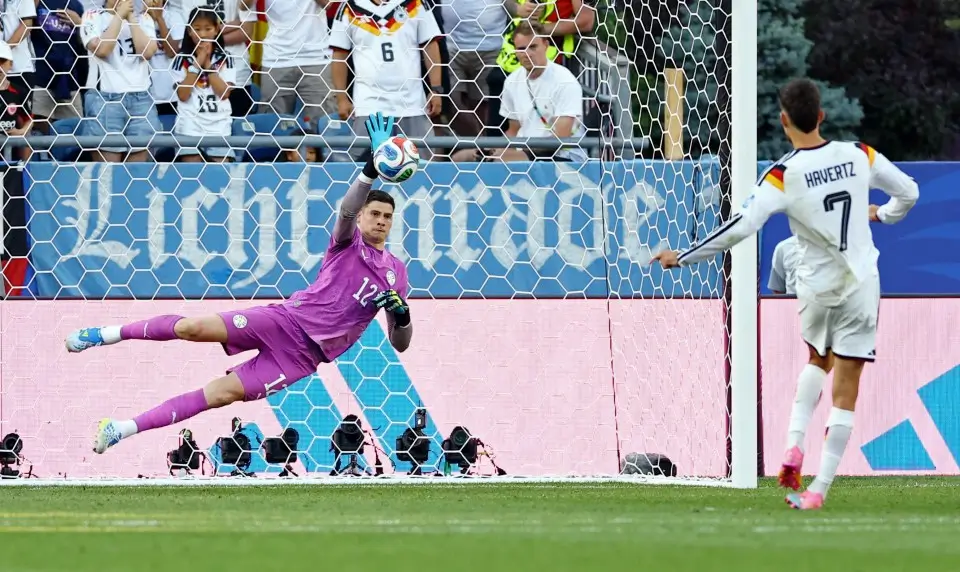 Germany goalkeeper dives to save a penalty during an international soccer match as Kai Havertz watches from the penalty spot.