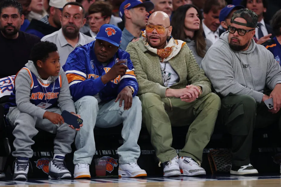 Courtside scene at a New York Knicks game featuring a group of spectators in Knicks apparel seated near the floor, engaged in conversation during the matchup