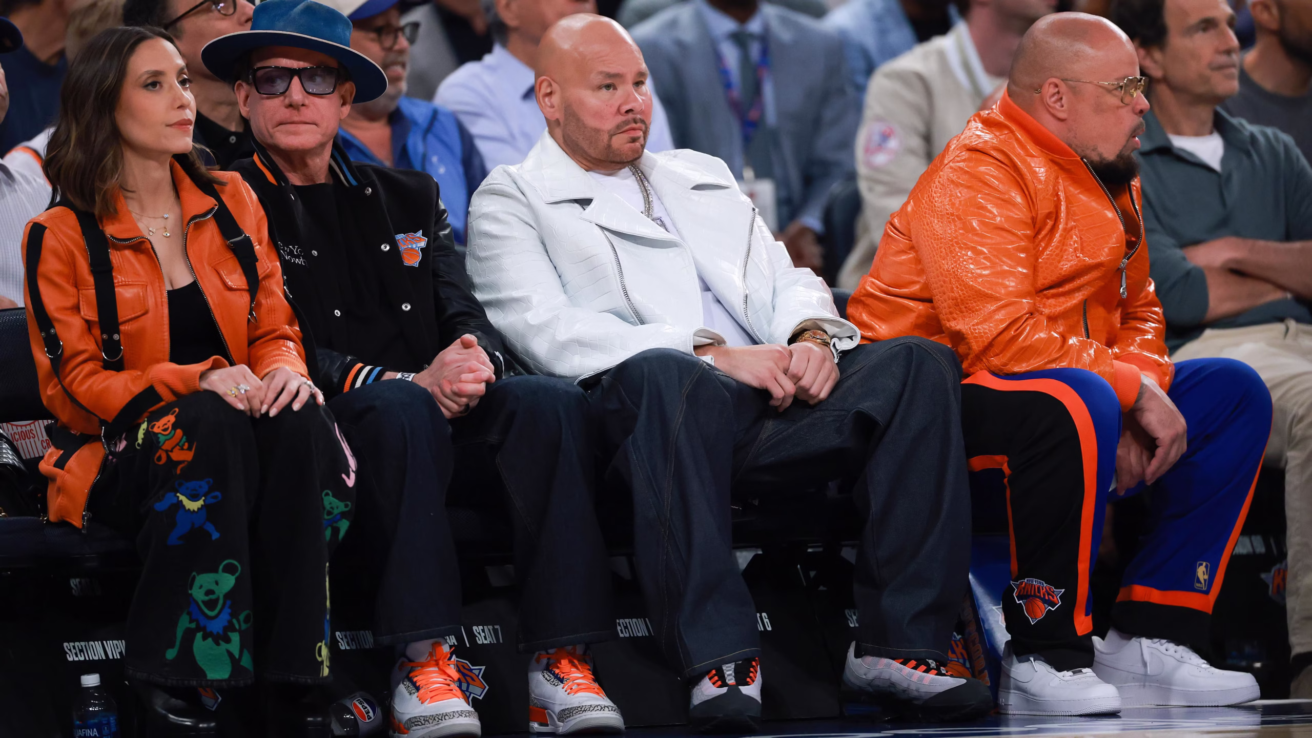 Front-row attendees at a New York Knicks game wearing bold fashion-forward outfits, including leather jackets, wide-leg trousers, and team-inspired orange-and-blue accent